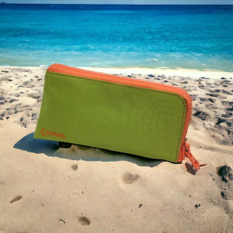Kühlende Insulin-Tasche in leuchtendem Grün liegt im Sand am Meer – sicherer Hitzeschutz für Diabetes-Medikamente im Sommerurlaub.